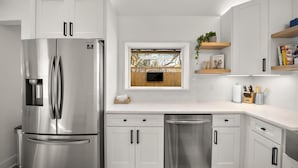 A modern kitchen with white cabinetry, stainless steel appliances, a window with a view of a wooden fence, and a countertop with kitchen tools. - * Gorgeous Loft Style House w/ Luxury, Charm, & Comfort * (Lutherville-Timonium)
