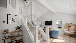 A staircase with white railings leading to a second floor, a mounted TV, a wicker chair, and a bookshelf with decorative items. - * Gorgeous Loft Style House w/ Luxury, Charm, & Comfort * (Lutherville-Timonium)