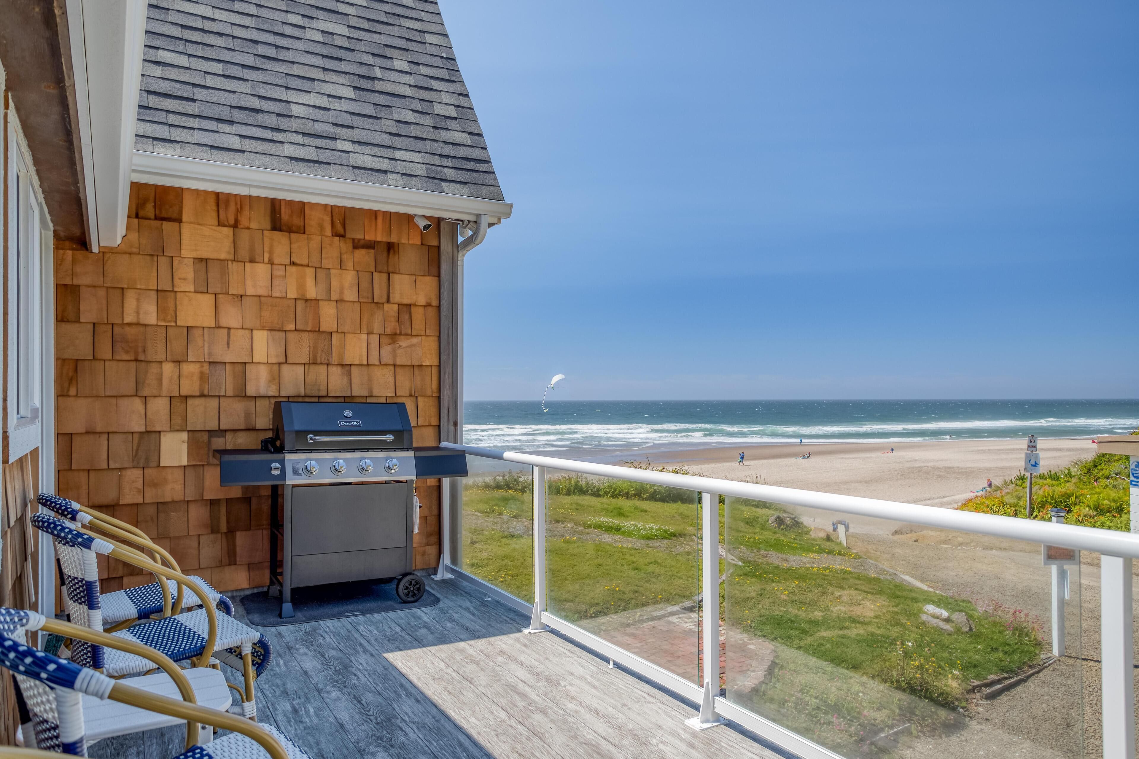 A balcony with a grill, wicker chairs, and a view of the beach.