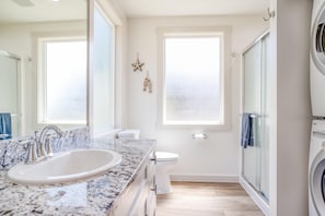 A modern bathroom with a marble sink, a toilet, a glass shower enclosure, and a washing machine. - Anchor Court (Lincoln City)