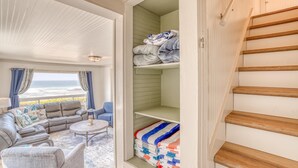 Un salon chaleureux avec vue sur l’océan, un meuble de rangement vert contenant des serviettes et un escalier en bois.
