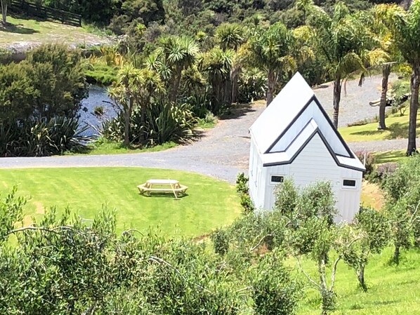 A white house with a triangular roof, surrounded by lush greenery and a small pond. - Beautiful & Unique - The Chapel at the Olive Grove (Russell)