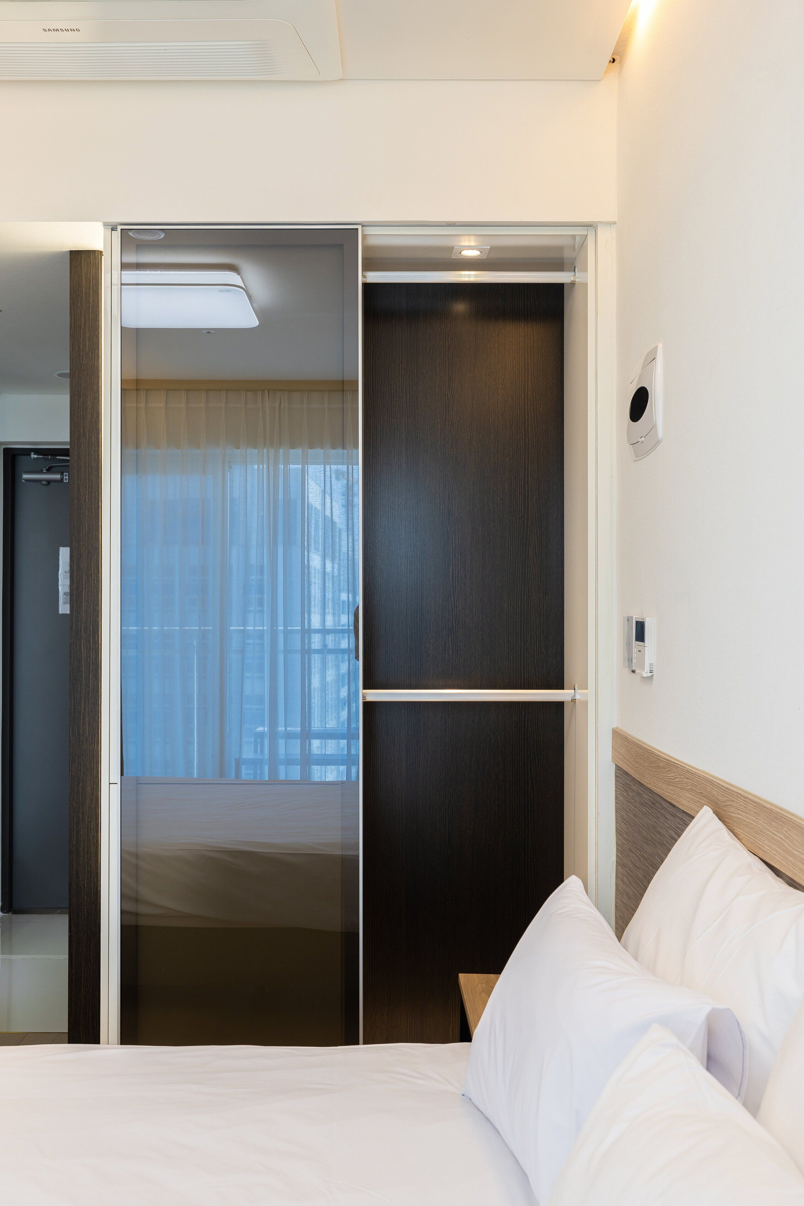 A hotel room with a bed, a sliding door closet, and a wall-mounted thermostat.