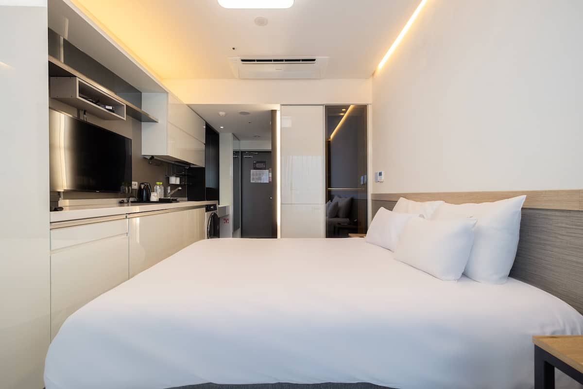 A modern hotel room with a large bed, a built-in kitchen, and a walk-in closet.