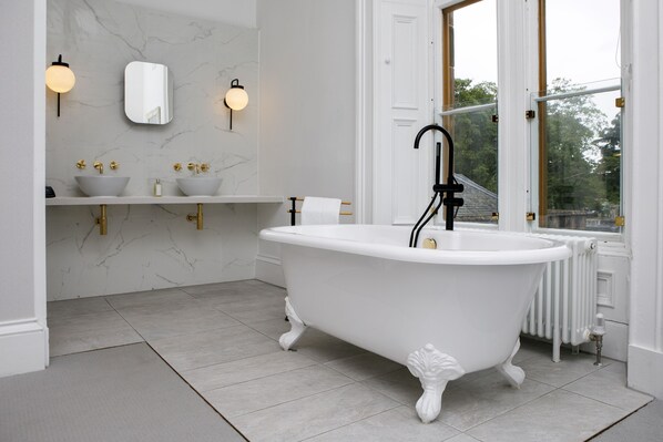 A bathroom with a freestanding bathtub, marble walls, and a window with a view of trees.