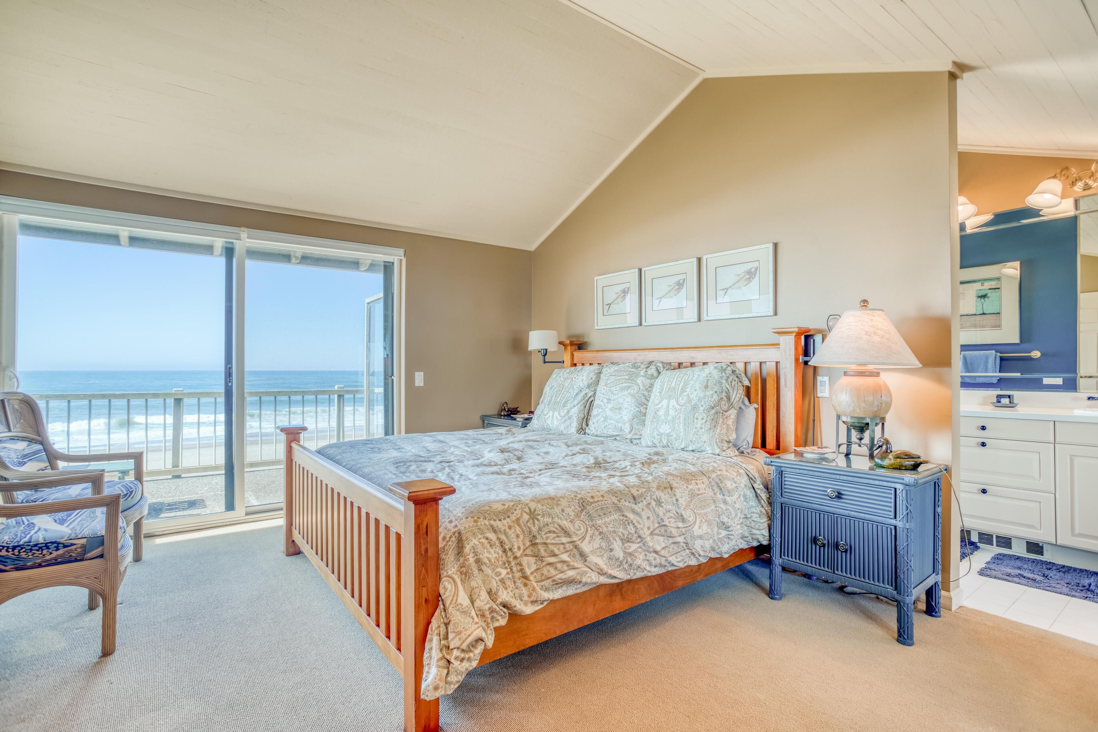 A bedroom with a large bed, a nightstand, a chair, and a view of the ocean.