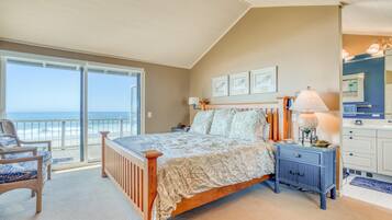 A bedroom with a large bed, a nightstand, a chair, and a view of the ocean.