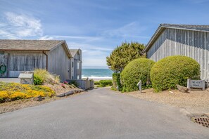 Una propiedad costera con un camino de entrada pavimentado que conduce a un edificio de madera, un letrero que indica un sendero hacia la playa y vista al océano.