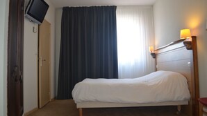 A hotel room with a bed, a television mounted on the wall, a window with curtains, and a bedside lamp. - Artyster Clermont-ferrand (Clermont-Ferrand)
