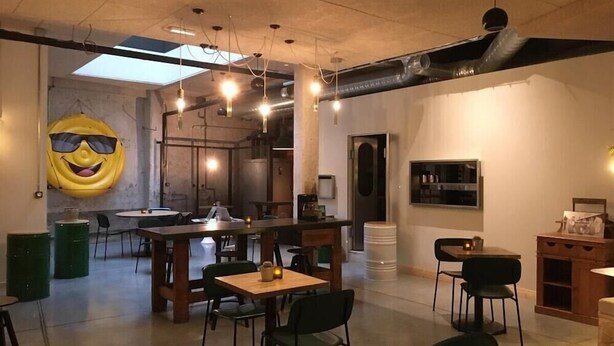 A modern dining area with tables and chairs, a large yellow smiley face decoration, and a visible door leading to another room. - Artyster Clermont-ferrand (Clermont-Ferrand)