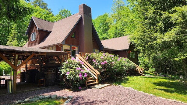 Un chalet rustique doté d’une terrasse en bois, d’un espace extérieur couvert avec des sièges et d’une allée en gravier.