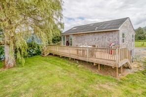 A wooden cabin with a deck, surrounded by grass and trees. - Nehalem House (Nehalem)