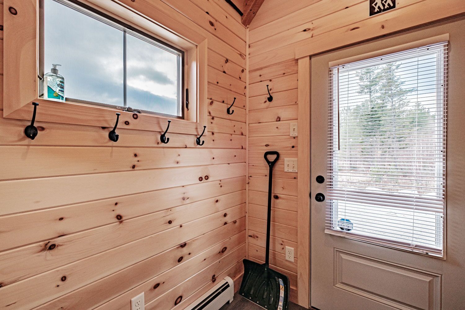 A wooden interior with a door, a window, and a broom leaning against the wall.