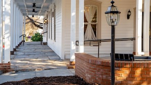 A covered porch with steps leading to a door, a brick wall, and a street lamp. - The Colonial Inn, an Ascend Collection Hotel (Hillsborough)