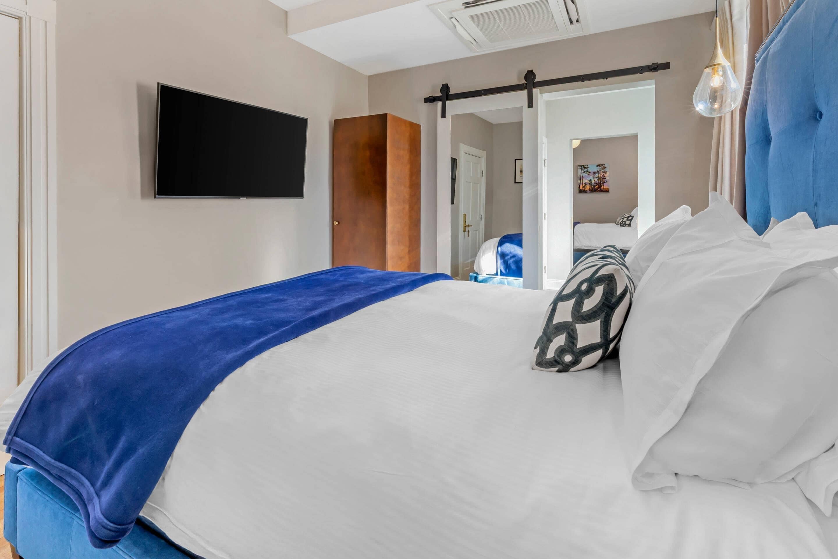 A hotel room with a bed, a TV mounted on the wall, a wardrobe, and a sliding door leading to another room.