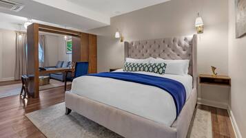 A modern bedroom with a large bed, a wooden desk, a chair, and a sofa.