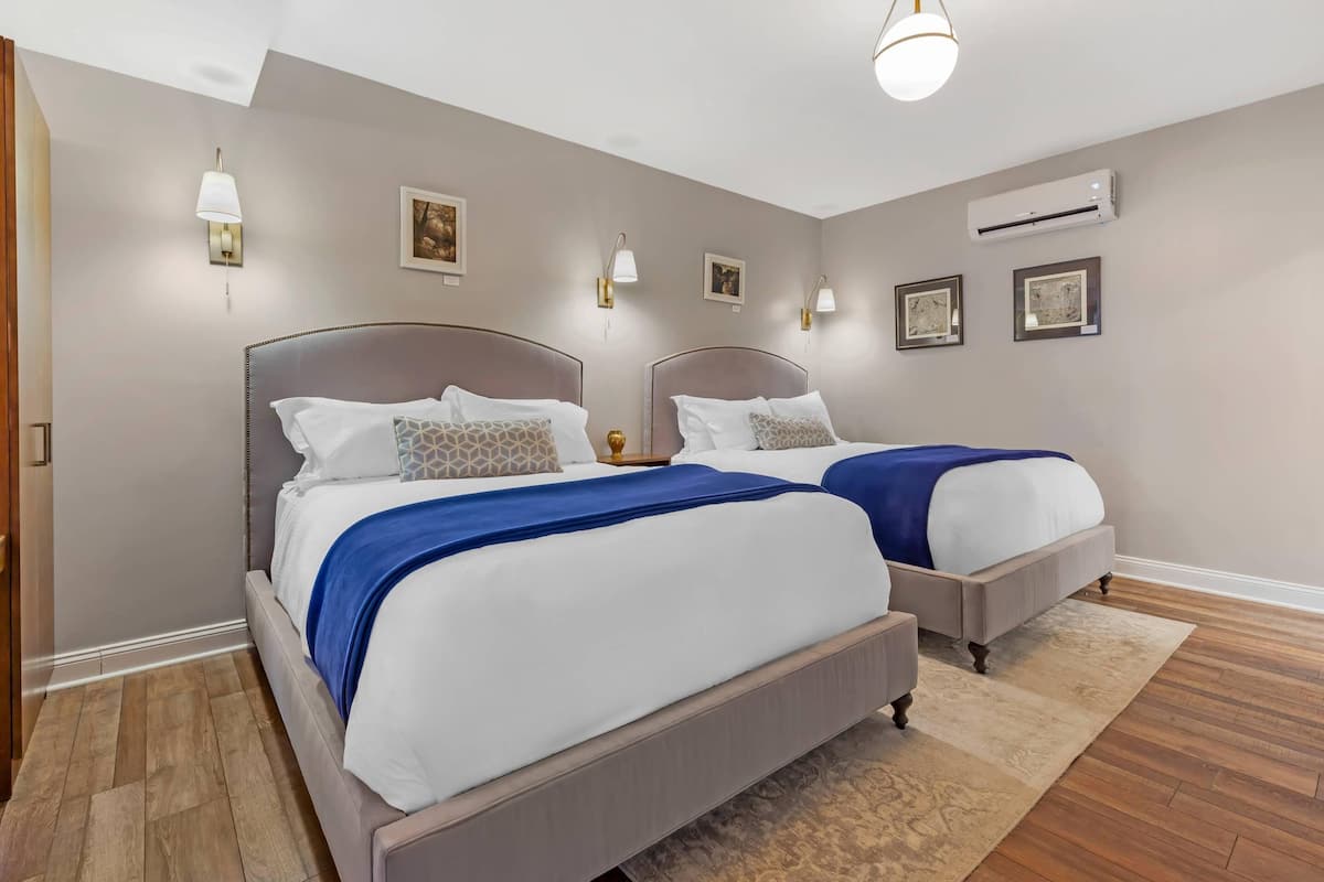 A bedroom with two beds, a wooden floor, and wall-mounted lighting.