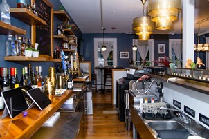 Uma área de bar com prateleiras de madeira, um quadro negro com o cardápio e diversas garrafas.