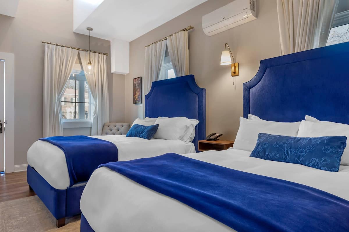 A hotel room with two beds, a nightstand, a lamp, and an air conditioning unit.