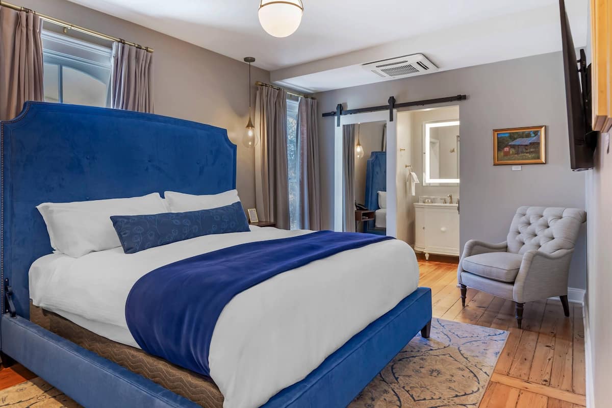 A bedroom with a large bed, a chair, a mirror, and a door leading to a bathroom.