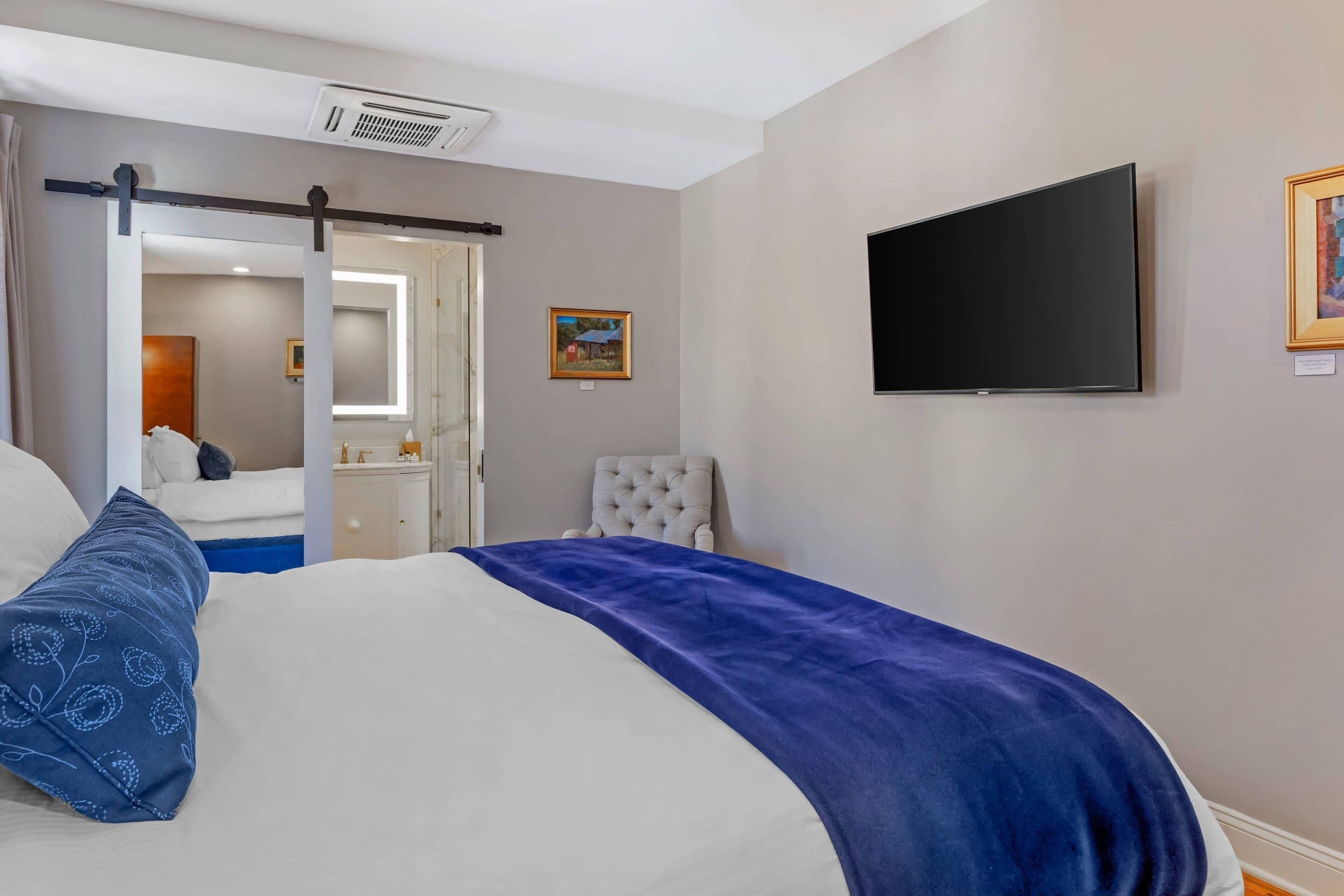 Une chambre d’hôtel comprenant un lit, une télévision, une chaise et une porte donnant accès à une salle de bain.