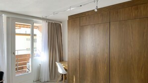 A modern room with a sliding glass door leading to a balcony, a wooden wardrobe, and a white chair. - Parkareal Apt 403 by Interhome (Davos)