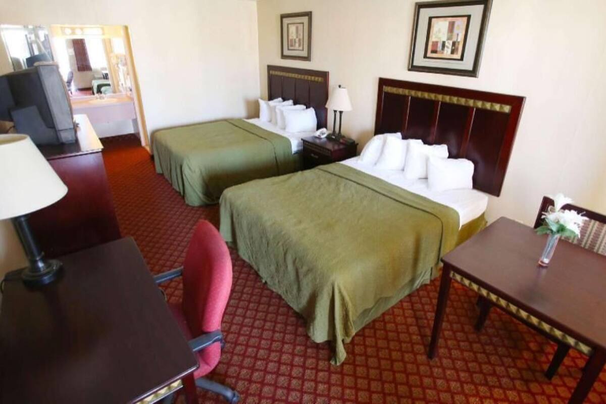 A hotel room with two single beds, a desk with a chair, a small table with a vase, and a mirror.