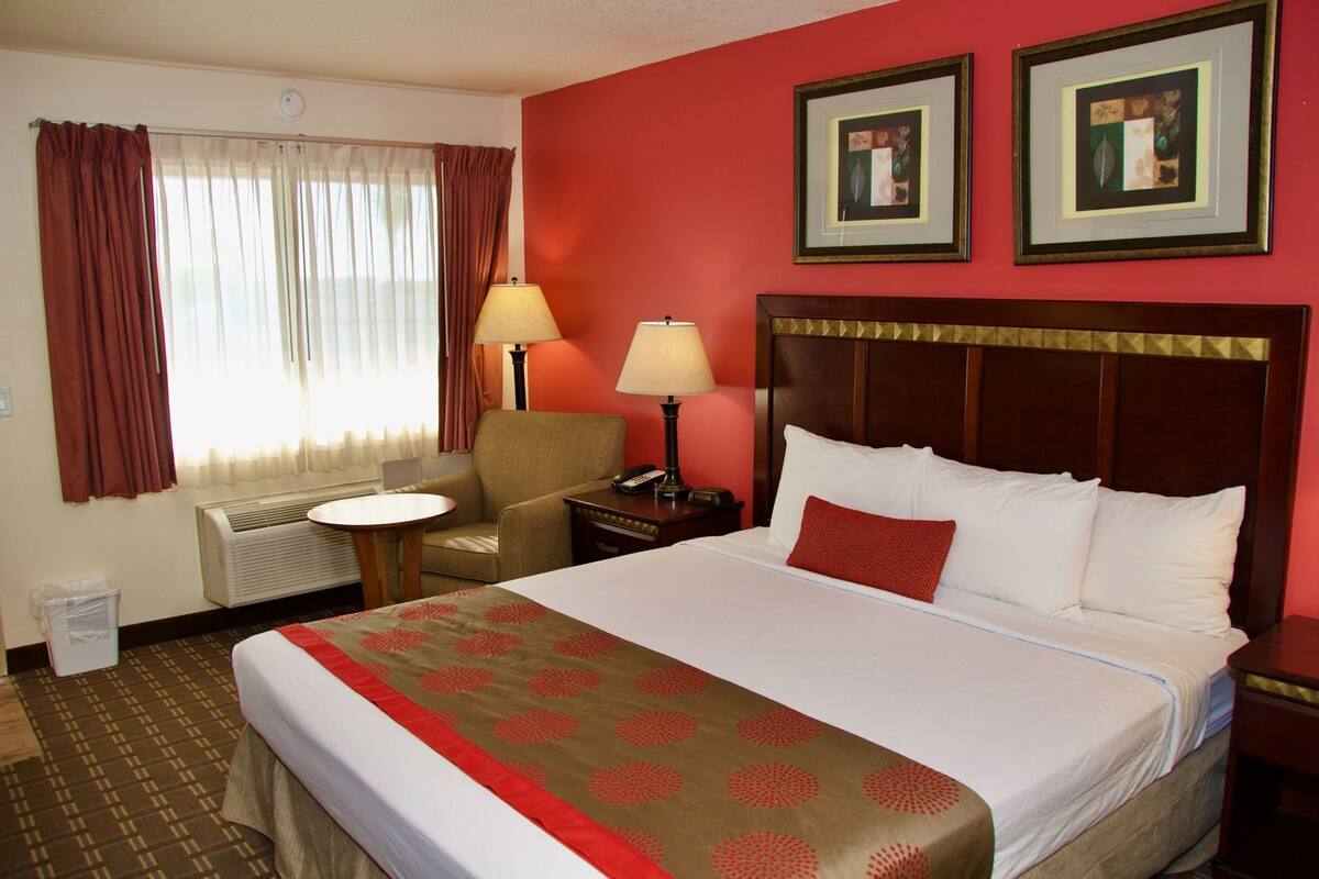 A hotel room with a large bed, a chair, a small table, two lamps, and a radiator.