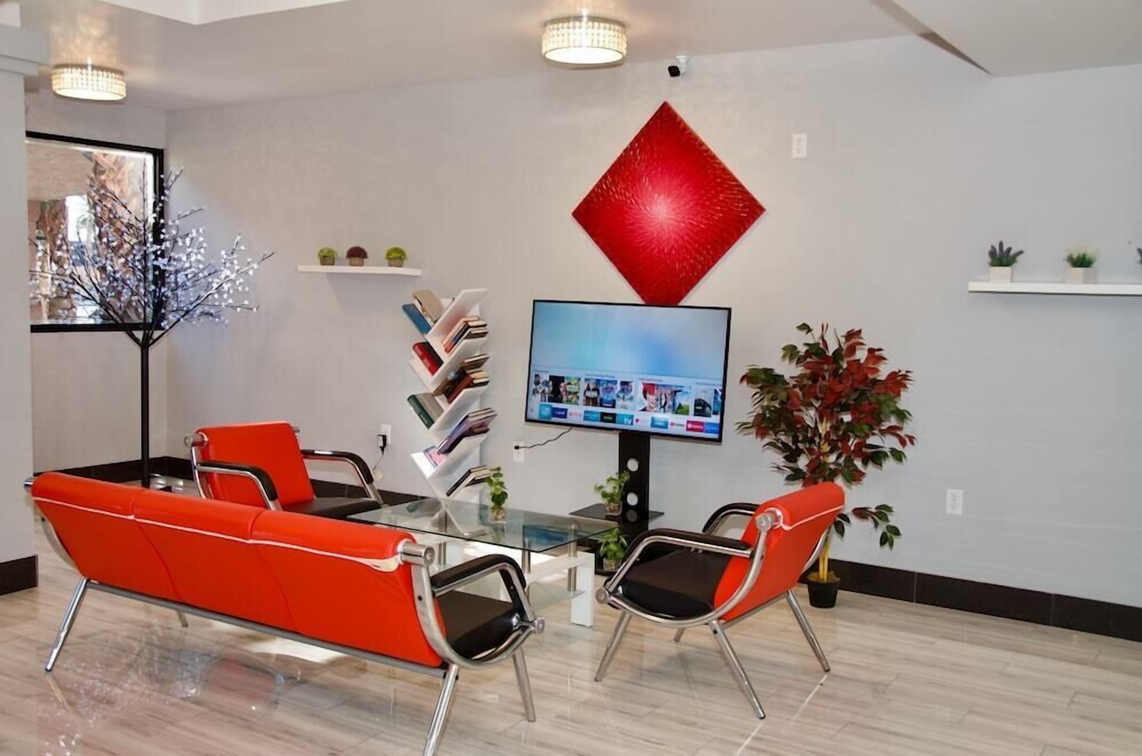 Een moderne kantoorruimte met een glazen tafel, rode stoelen, een grote televisie en decoratieve planten.