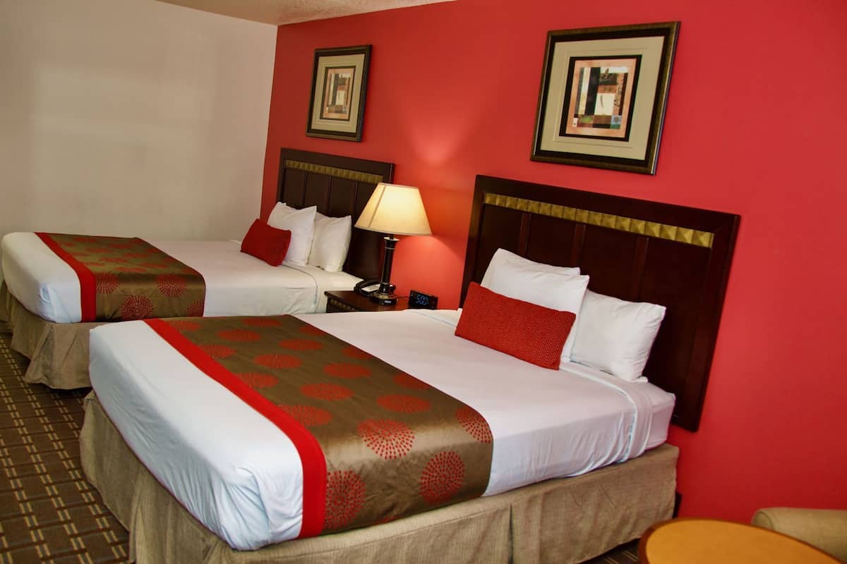 A hotel room with two beds, a nightstand with a lamp, and two framed pictures on the wall.
