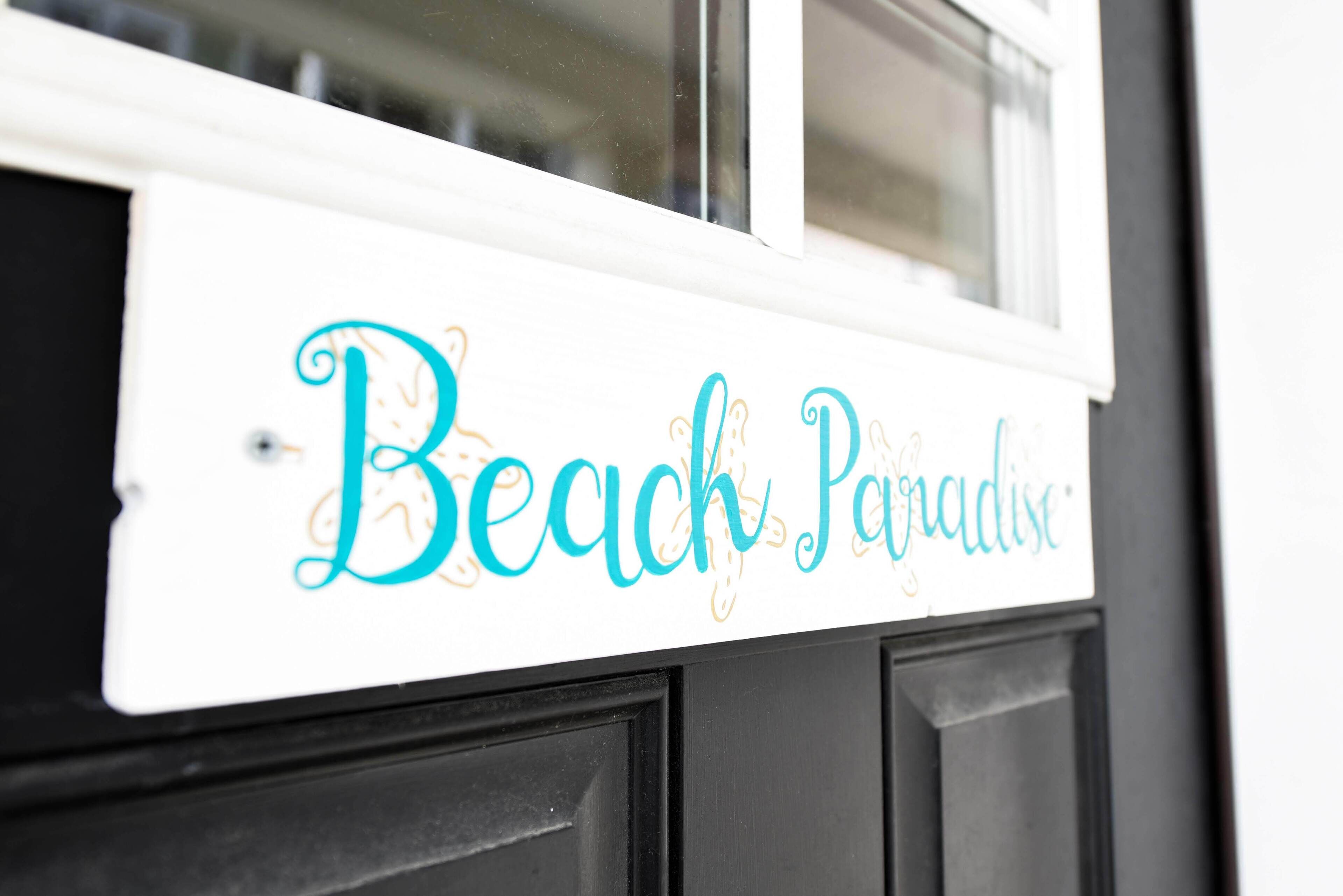 Un panneau blanc sur lequel on peut lire, en lettres cursives bleues, les mots « Beach Paradise ».