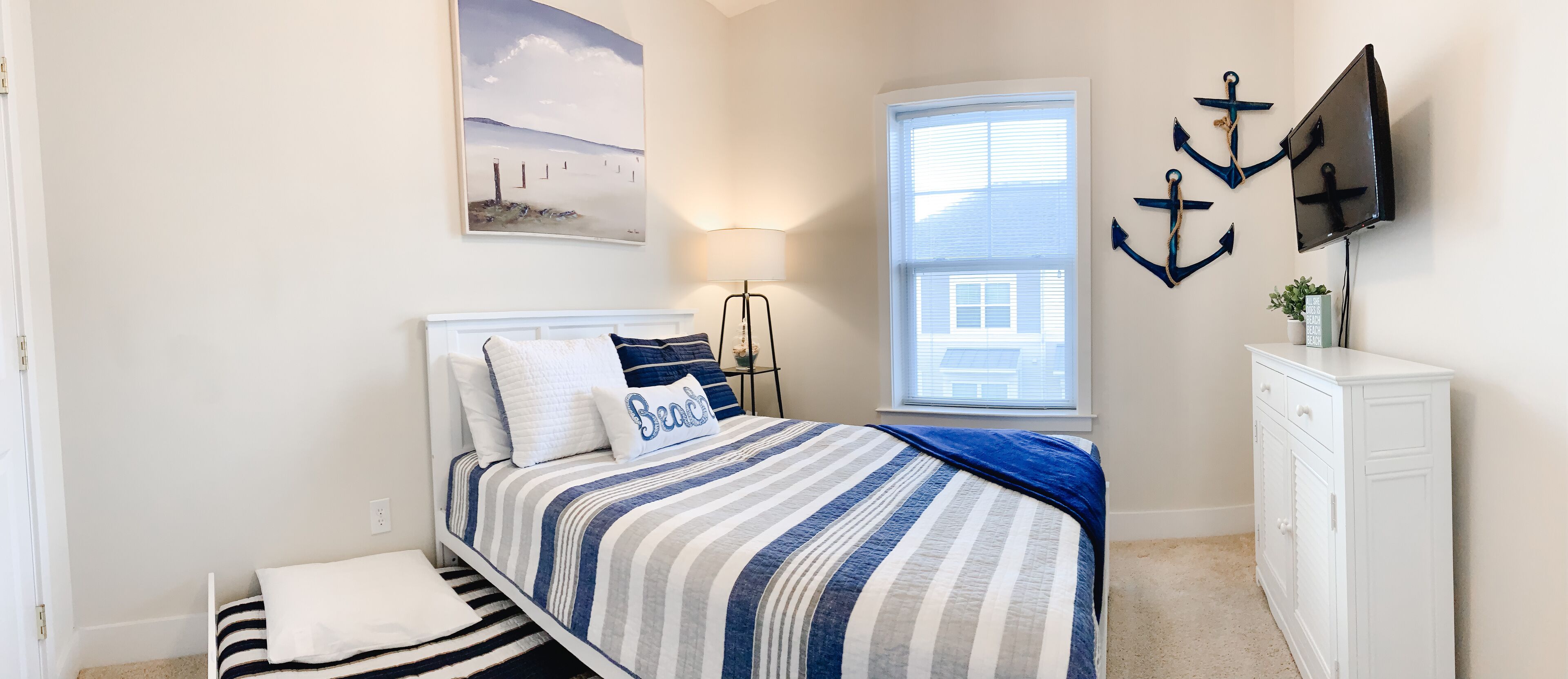 A bedroom with a bed, a nightstand, a lamp, a TV, and a window.