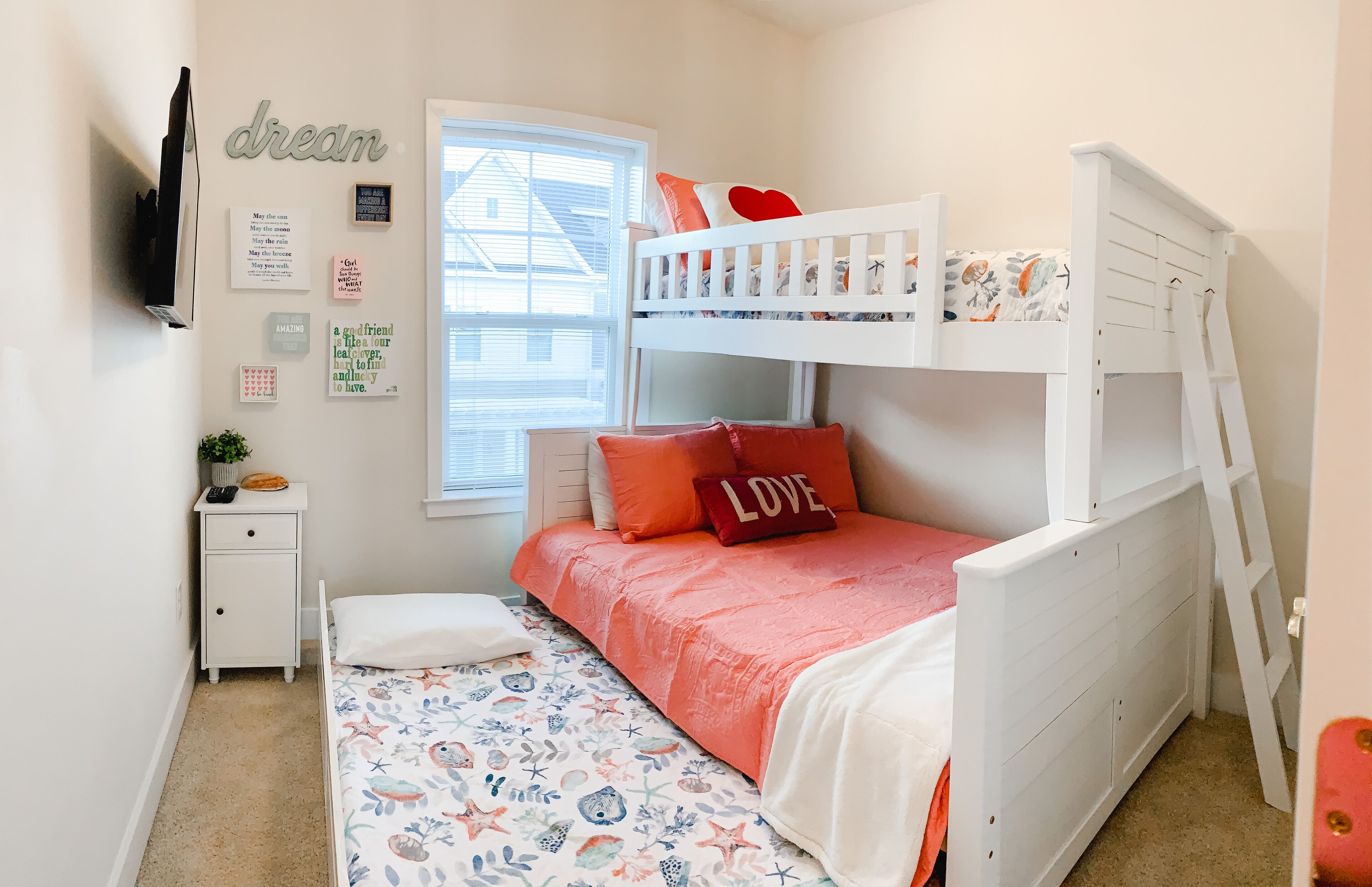 A child's bedroom with bunk beds, a white nightstand, a window, and motivational wall art.