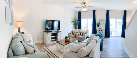 A modern living room with a flat-screen TV, a sofa, a coffee table, and a staircase leading to an upper floor.