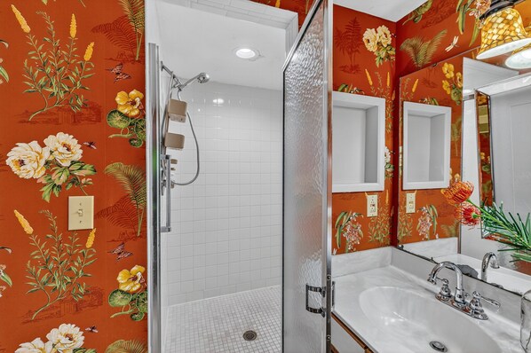 A bathroom with a shower, a sink, and a mirror. The walls are decorated with floral wallpaper. - Oceanfront Condominium with Great Amenities (St Simons)