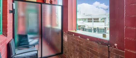 Un balcón con puerta de vidrio, una silla de mimbre y vista a un edificio de fachada blanca.