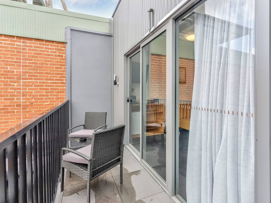 A balcony with a wicker chair and table, a sliding glass door, and a brick wall.