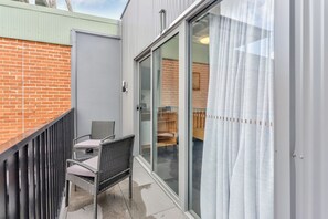 A balcony with a wicker chair and table, a sliding glass door, and a brick wall. - Meridian Hotel (Hurstville)