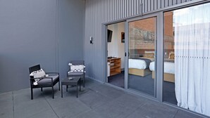Una habitación de hotel moderna con una puerta de cristal corredera que da a un balcón con dos sillas y una mesita.