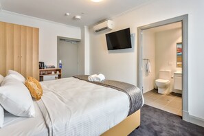 A hotel room with a bed, a TV mounted on the wall, a wardrobe, a small kitchenette, and a bathroom with a toilet and sink. - Meridian Hotel (Hurstville)