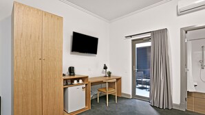 Habitación compacta con armario de madera, pequeña kitchenette, escritorio con silla, televisor de pantalla plana y puerta corrediza de vidrio a un área exterior.