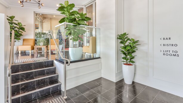 Un moderno vestíbulo de hotel con una escalera de cristal, un bar, un ascensor a las habitaciones y un bistró.
