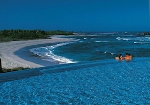 Relax by the serene pool overlooking the adjacent beach with its gentle waves and lush green surroundings.