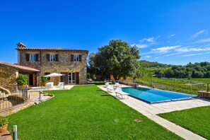 A stone villa with a swimming pool, a well-maintained lawn, and a vineyard in the background.