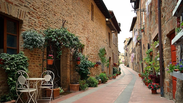 Une ruelle étroite bordée d’immeubles en briques, avec des tables et des chaises installées à l’extérieur et des plantes en pot.