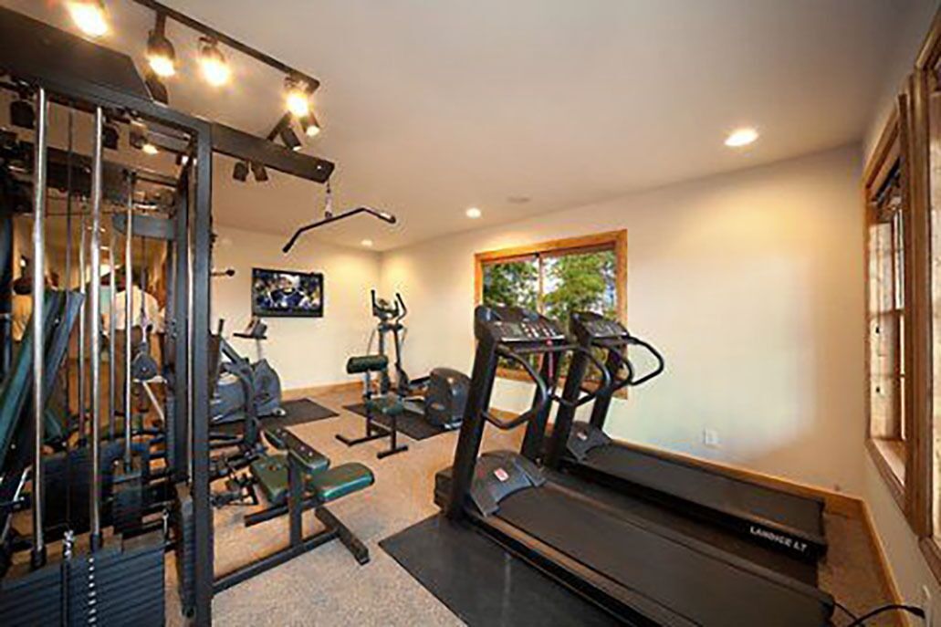 A home gym with a treadmill, weight bench, and various exercise machines.