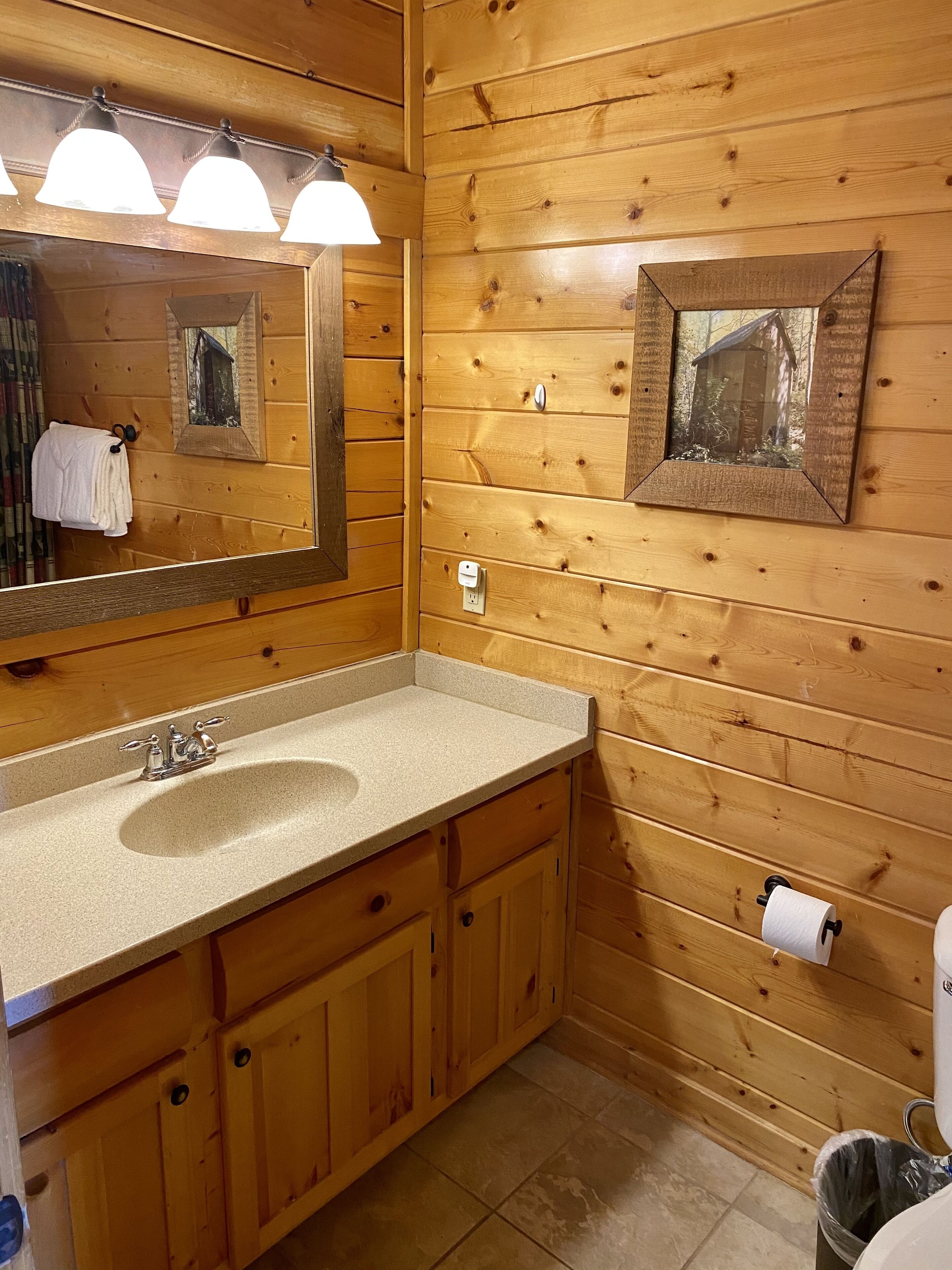 Un baño de madera con lavamanos, espejo, toallero y un cuadro enmarco.