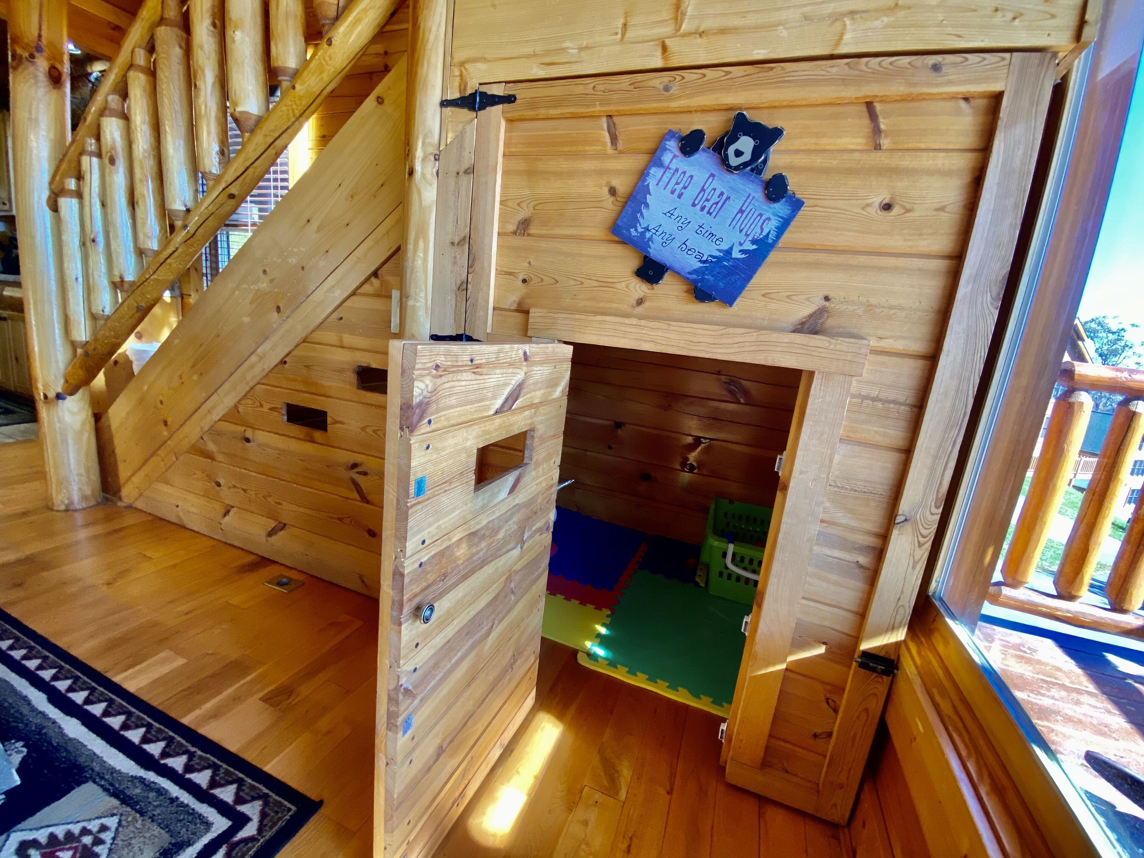 Interior de madeira com escada, área de recreação com escorrega e porta de madeira decorada com um urso.