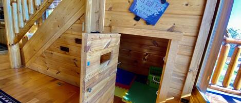 A wooden interior with a staircase, a play area with a slide, and a wooden door with a bear decoration.