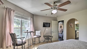 Un dormitorio con una cama, ventilador de techo, televisión y ventana con cortinas.